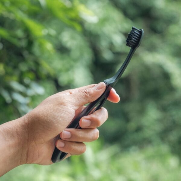 megasmile Loop Zahnbürste mit Aktivkohle-Borsten. Abbildung Zahnbürste black in der Hand, draussen im grünen.